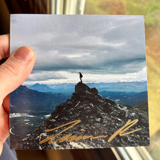 Hand holding signed CD with a mountain scene.
