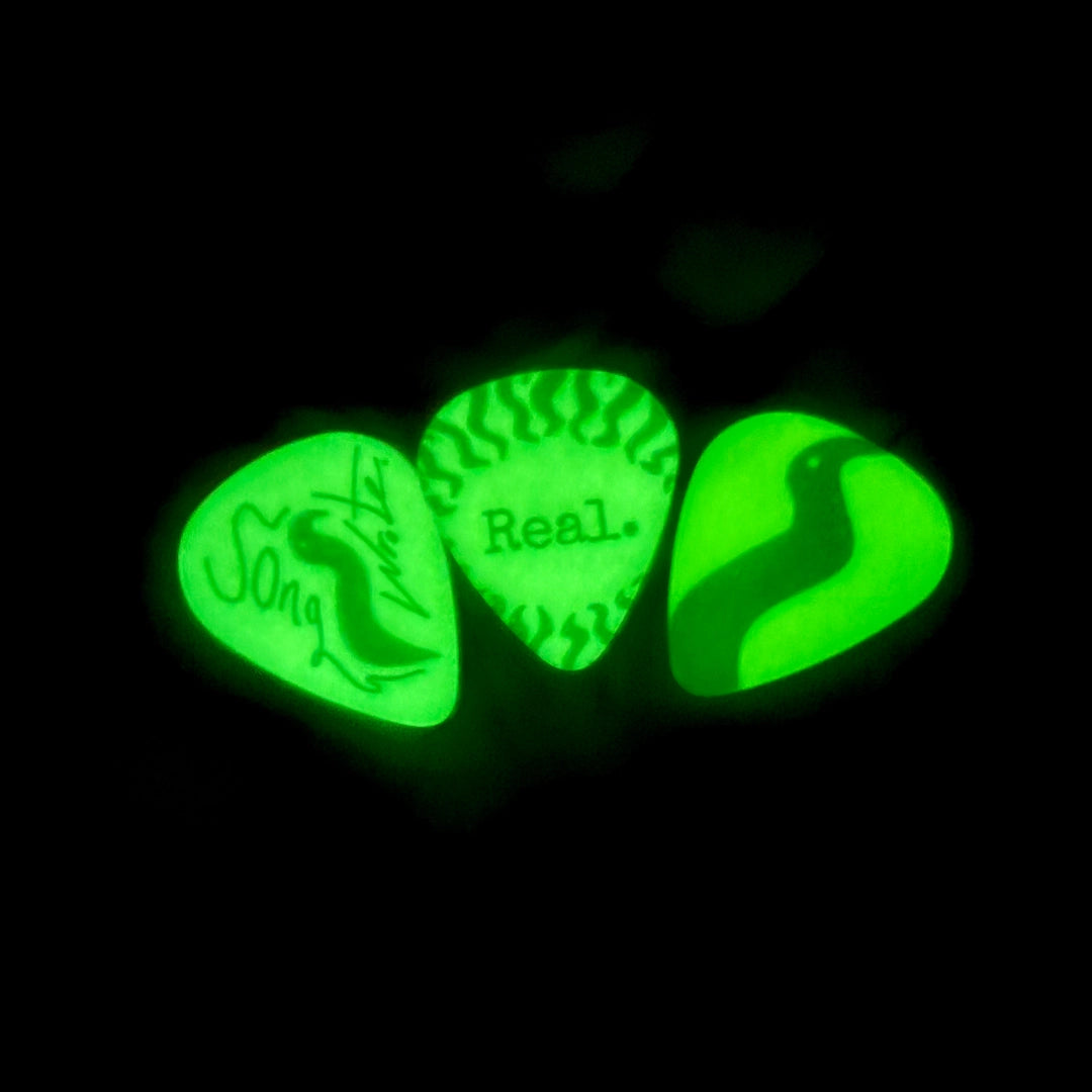 Three glow-in-the-dark guitar picks on a black background.