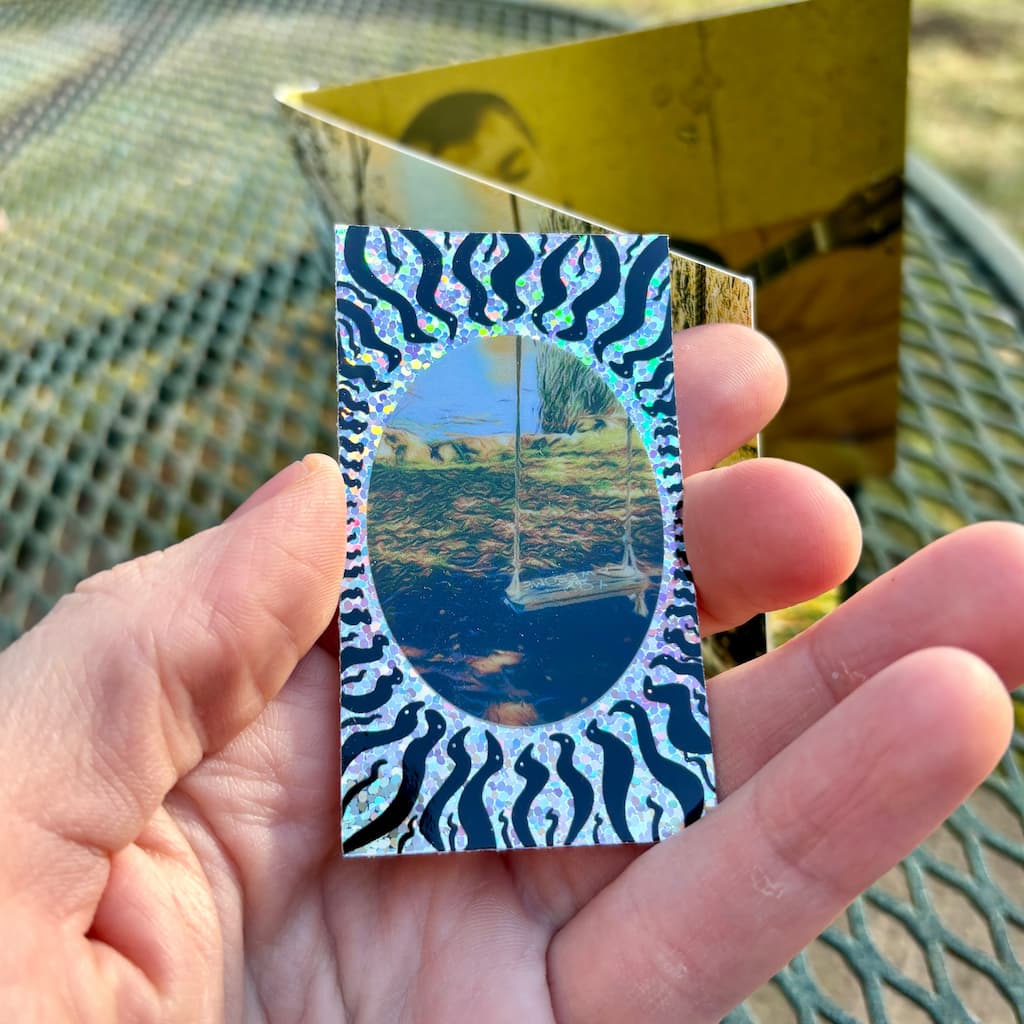 Hand holding a rectangular shiny glitter sticker with album art.