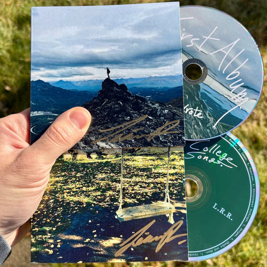 Two CD wallets with mountain and swing scene held by a hand, with two CDs inside.