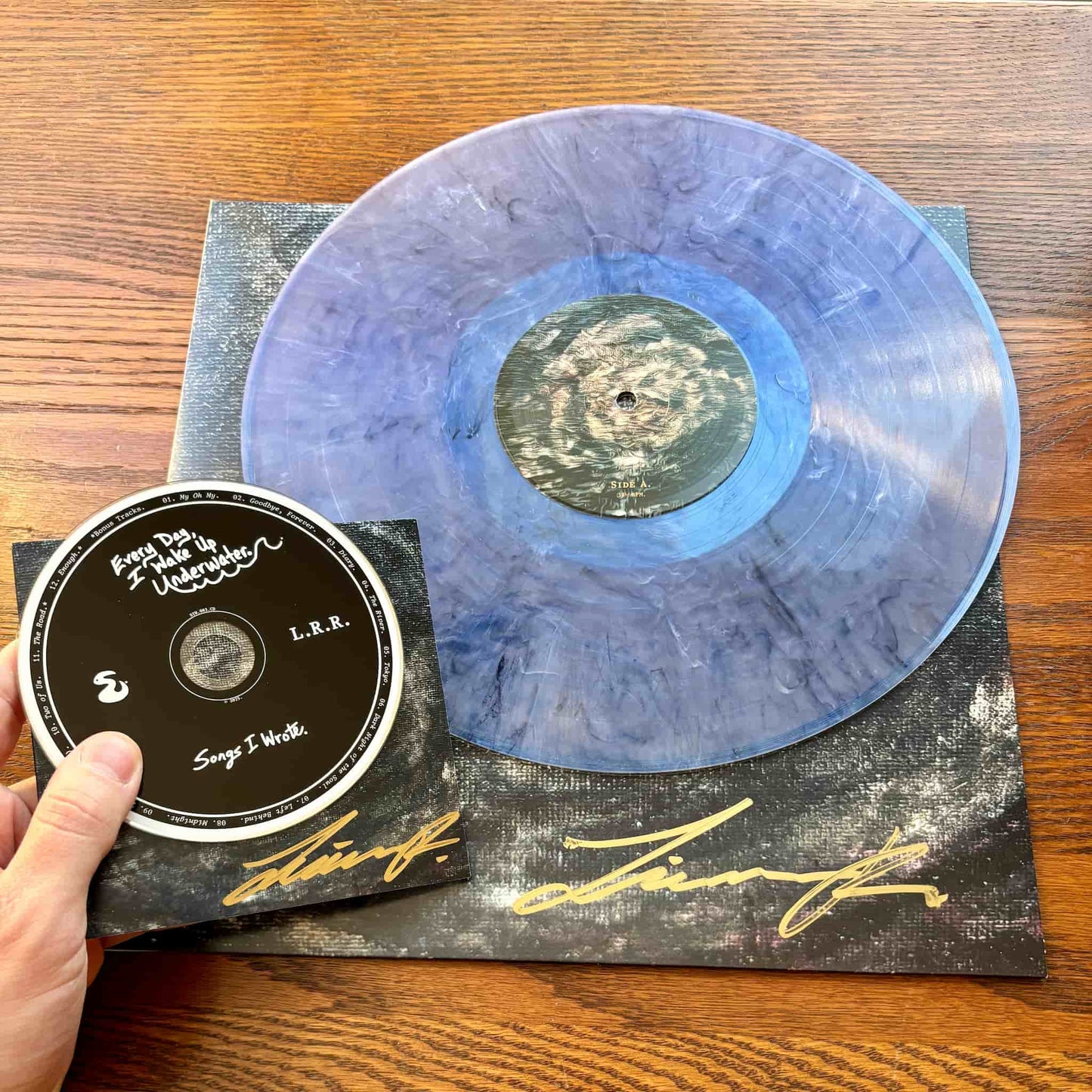 Blue vinyl record with a black label and signed CD copy on a wooden surface